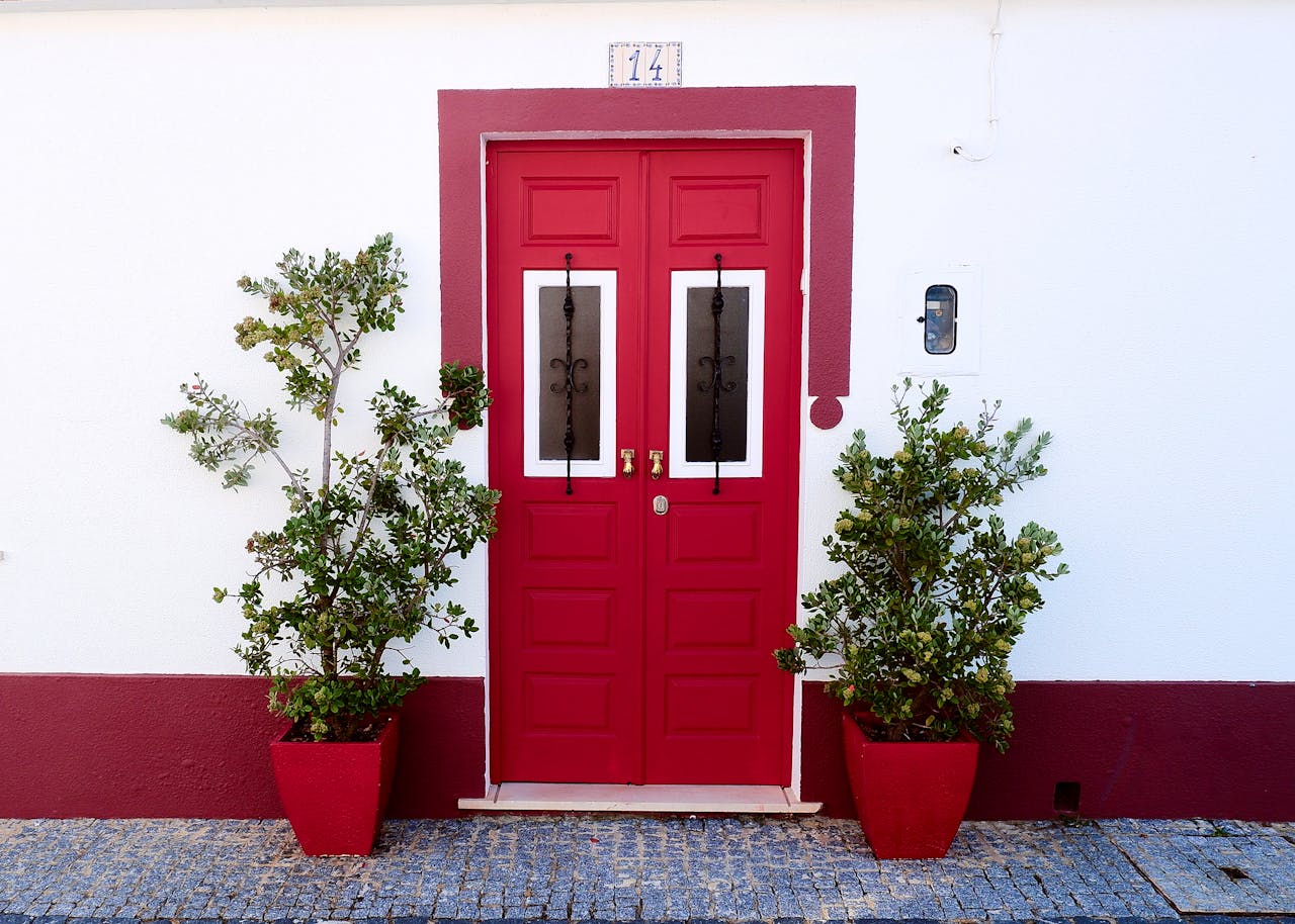 Vibrant red door with potted plants in a traditional Portuguese setting.